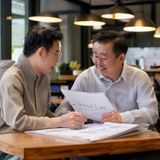 黄油作坊创业导师陈立明，成熟男性，正在与学员讨论黄油作坊开店方案，桌上摆放着商业计划书