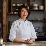 黄油作坊创始人林晓奶，短发女性，身着白色围裙站在工坊操作台前，神情专注而温和